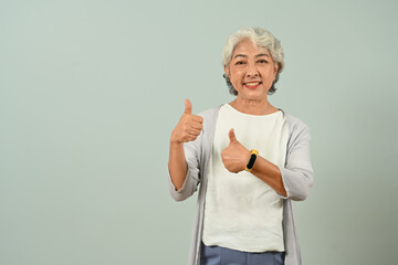 Beautiful 60s woman making thumbs up, approving, positive gesture, standing over blue background