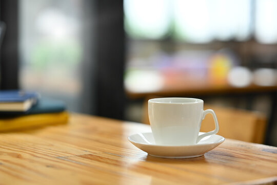 Closeup white cup of coffee and books on wooden office desk. Empty area left side of image for your text