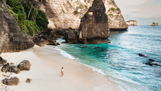 Podr&oacute;żnik idący po pięknej plaży Diamond, na Indonezyjskiej wyspie Nusa Penida, plaża, skały klif oraz ocean.