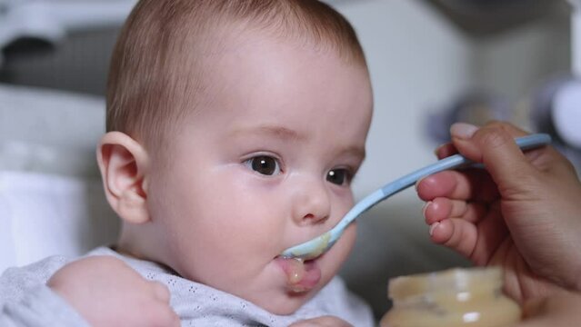 adorable baby eating mashed puree food with spoon.mother mom woman feeding toddler infant child.hungry boy food diversification first solid meal 4k.child in swing crib
