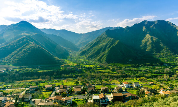 landscape of green summer highland mountain range with green beautiful valley with nice town below and amazing blue cloudy sky