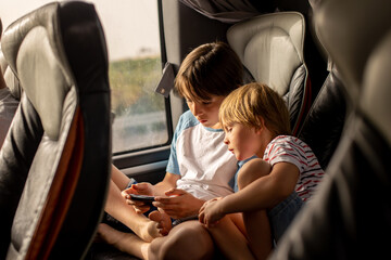 Children, siblings, playing on a mobile phone while traveling with bus on a long trip journey