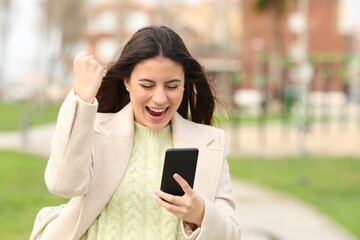 Excited woman checking smart phone content in a park