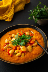 Healthy lunches, tomato and carrot puree soup, beans with pumpkin seeds, healthy tasty legumes, view of a plate of soup on a black background
