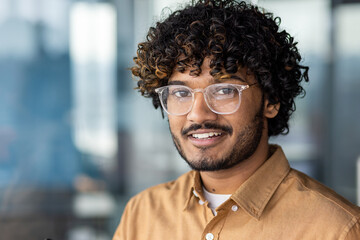 Close-up portrait of young hispanic man wearing glasses, man smiling and looking at camera at...