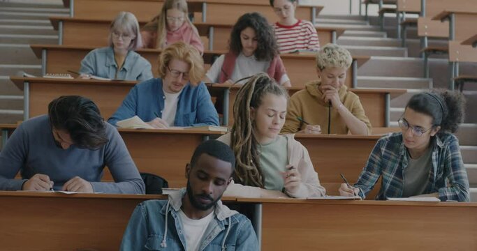Multicultural group of men and women students writing test concentrated on examination in classroom in college. Education and youth concept.