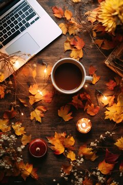Autumn - themed flat lay with a laptop, notebooks, and a mug of hot apple cider on a desk, surrounded by golden fall leaves