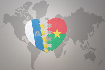 puzzle heart with the national flag of burkina faso and canary islands on a world map background.Concept.