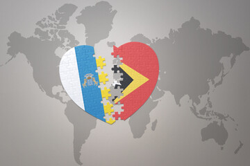 puzzle heart with the national flag of east timor and canary islands on a world map background.Concept.