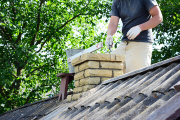 Chimney construction, repairs and re-building. A contractor is bricklaying a brick chimney on an...