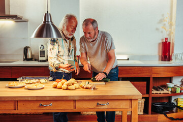 Two senior men using kitchen together.