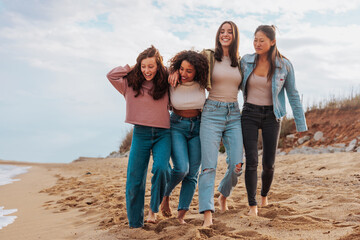 Friendship group of four diverse young women walking together on beach