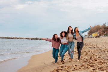 Diverse young women running and jumping on beach together