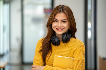 Young Beautiful smiling happy student woman wearing headphone holding a book, Portrait of student girl carry book balancing books on head and hand