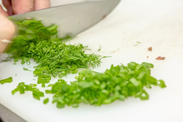 Close-up of a chef hands cutting green onions on a cutting board with a knife for preparing vegetarian food.