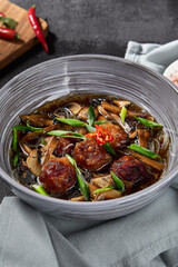 Asian-inspired soup boasting mushrooms and meatballs, artistically presented on a black backdrop with vibrant fresh ingredients. An elegant textile napkin completes the enticing culinary display