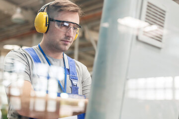 Focused worker in protective workwear at computer in factory