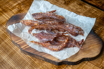 Pieces of dried meat on paper on a stand on the table