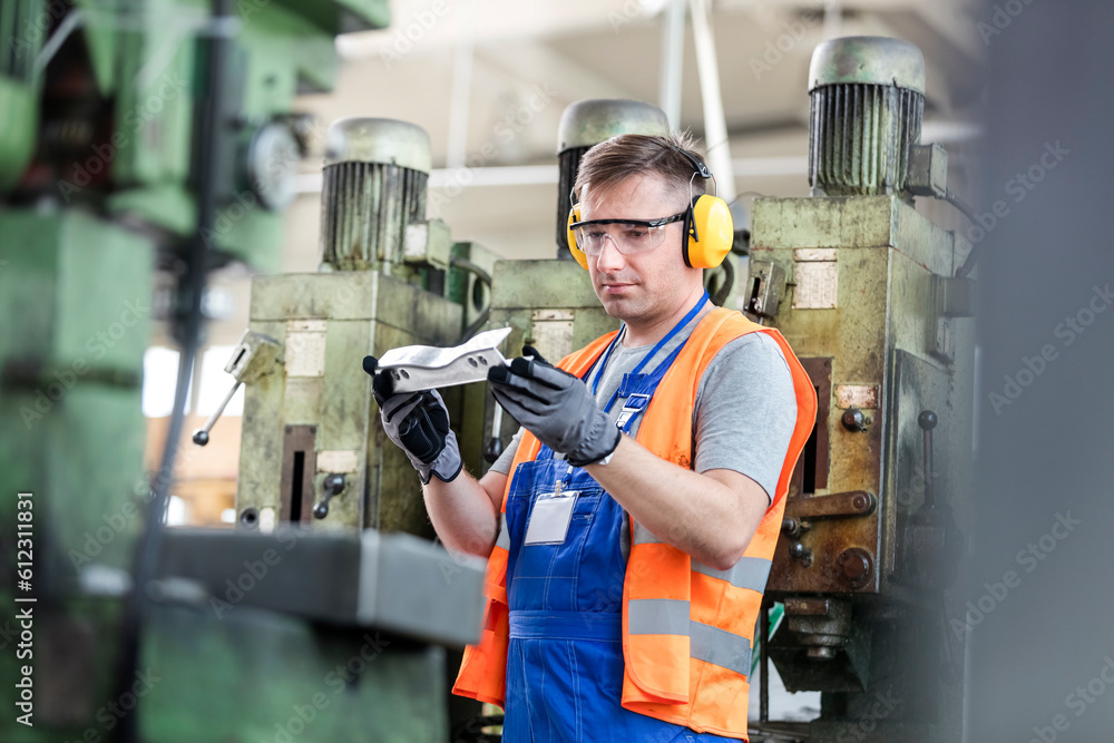 Poster Worker in protective workwear examining part in factory