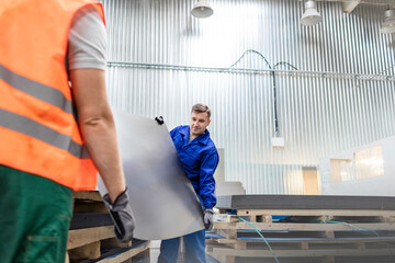 Workers carrying sheet metal in factory