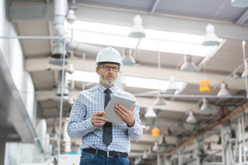 Engineer with hard-hat and digital tablet walking in factory