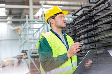 Worker in protective workwear clipboard examining steel parts in factory