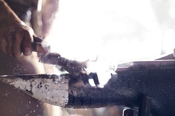 Close up of blacksmith brushing iron tool over anvil in forge