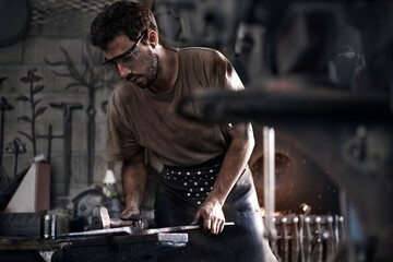 Blacksmith hammering iron at anvil in forge