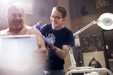 Smiling man with digital tablet getting shoulder tattoo