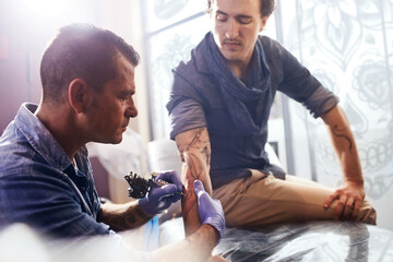 Tattoo artist tattooing man‚Äôs forearm