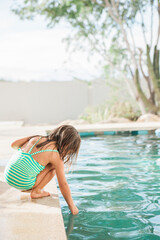 Toddler girl testing the water at edge of swimming pool