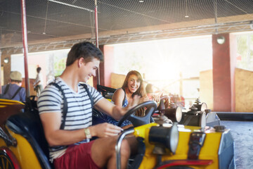 Young couple riding bumper cars at amusement park