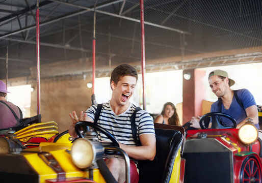 Laughing young men riding bumper cars at amusement park