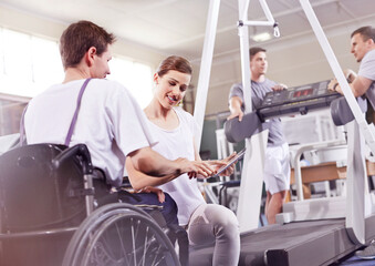 Physical therapist showing digital tablet to man in wheelchair - obrazy, fototapety, plakaty
