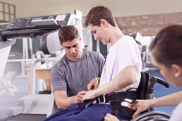 Fototapeta na wymiar Physical therapists attaching equipment to man in wheelchair