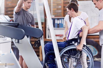 Physical therapists helping man in wheelchair onto treadmill - obrazy, fototapety, plakaty