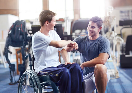 Physical therapist fist bumping man in wheelchair