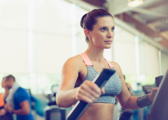 Fototapeta na wymiar Focused woman exercising on elliptical trainer in gym