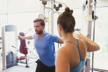 Female personal trainer guiding man doing cable chest fly at gym
