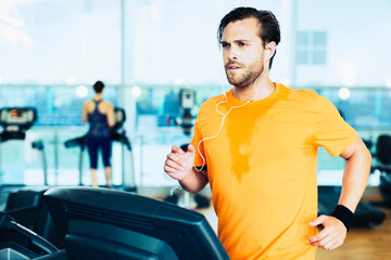 Sweating man with headphones running on treadmill at gym