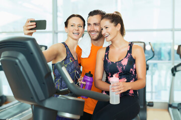 Smiling friends taking selfie at exercise bike in gym