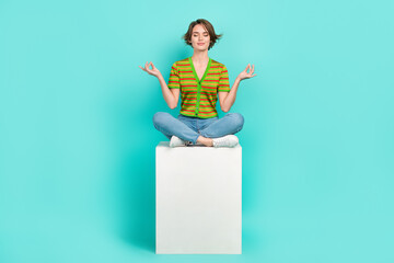 Full length photo of calm peaceful person sit podium cube meditate isolated on teal color background