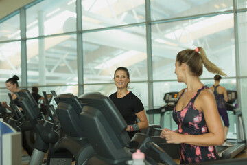 Fototapeta na wymiar Smiling women talking and jogging on treadmills at gym