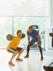 Personal trainer guiding man doing barbell squats at gym