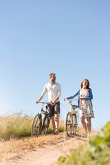 Young couple walking bicycles on dirt road below sunny blue sky