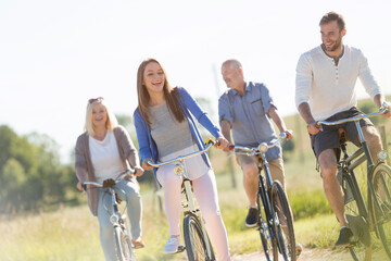 Happy family bike riding in sunny field - obrazy, fototapety, plakaty