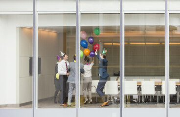 Playful business people in party hats celebrating balloons in conference room