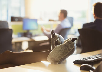 Businesswoman wearing wolf paw slippers with feet up on office desk