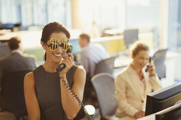 Portrait smiling businesswoman wearing dollar sign sunglasses answering telephone in office