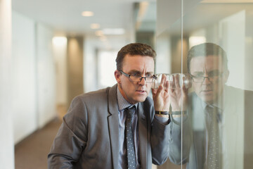 Focused businessman eavesdropping with glass in office corridor